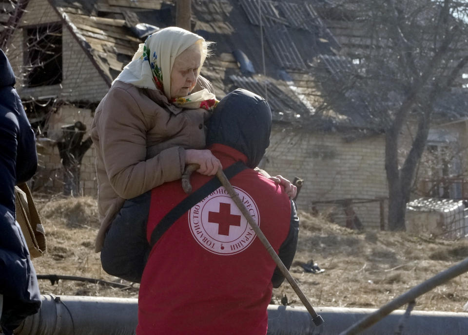 A Red Cross worker carries an elderly women during evacuation in Irpin, some 25 km (16 miles) northwest of Kyiv, Friday, March 11, 2022. Kyiv northwest suburbs such as Irpin and Bucha have been enduring Russian shellfire and bombardments for over a week prompting residents to leave their home. (AP Photo/Efrem Lukatsky)