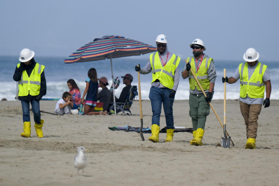 FILE - In this Oct. 11, 2021, file photo, a family, background, is under an umbrella as workers continue to clean the contaminated beach in Huntington Beach, Calif. California's uneasy relationship with the oil industry is being tested again by the latest spill to foul beaches and kill birds and fish off Orange County. (AP Photo/Ringo H.W. Chiu, File)