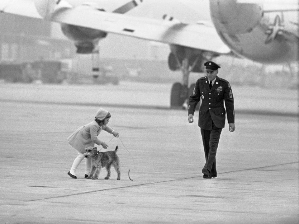 Caroline Kennedy with her dog Charlie on the tarmac in front of a plane after having caught him running away at the airport in 1963.