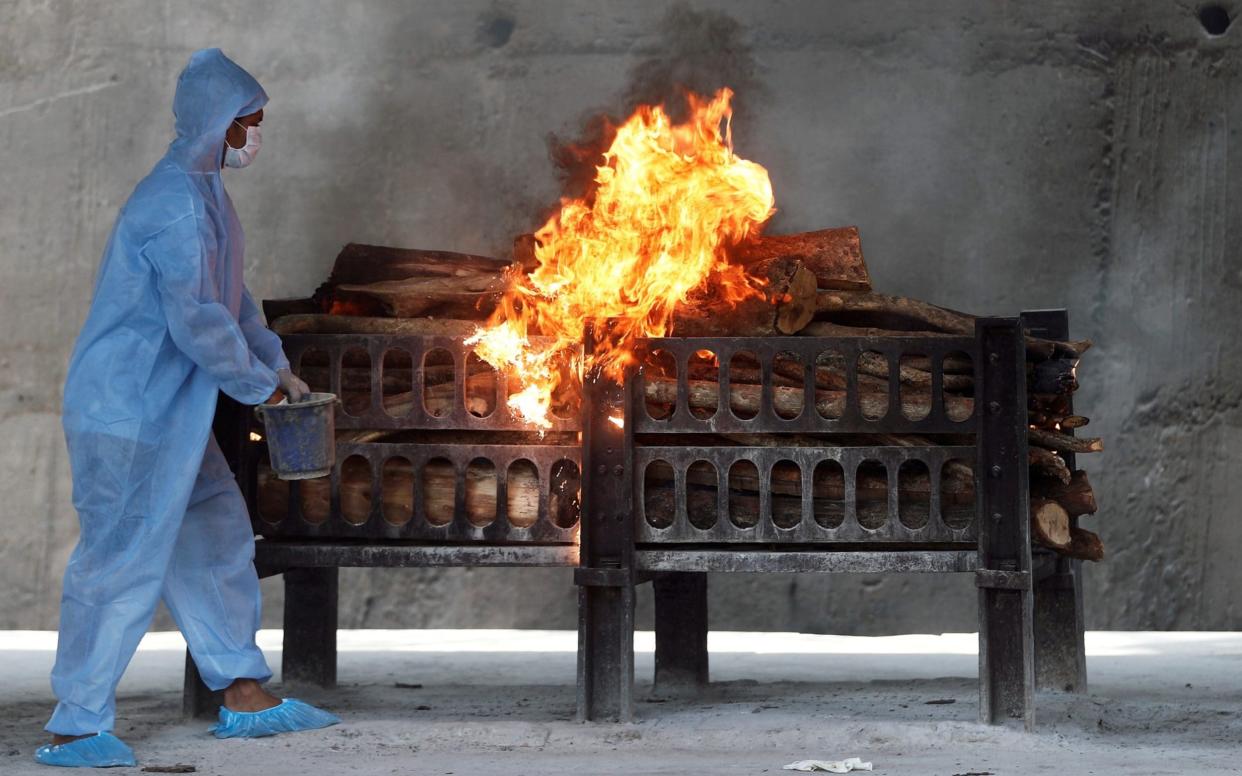 A frontline worker in PPE sprays a flammable liquid on a burning funeral pyre for a coronavirus victim - Reuters