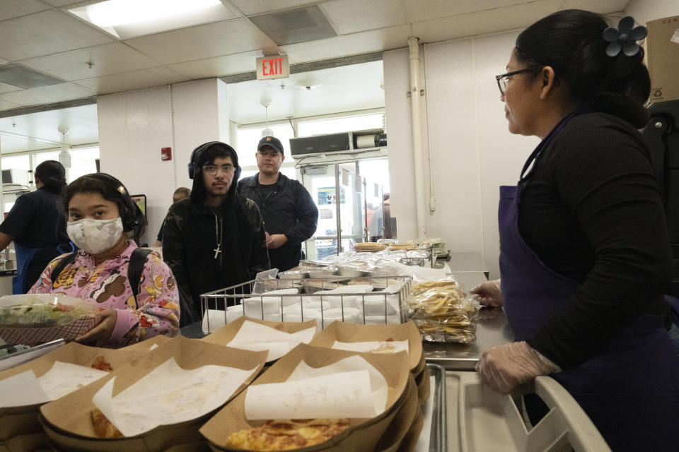 Cafeteria worker Claudia Rodriguez, right, serves students lunch at Firebaugh High School in Lynwood, Calif. on Wednesday, April 3, 2024. Demand for school lunches has increased after California guaranteed free meals to all students regardless of their family's income. Now, districts are preparing to compete with the fast food industry for employees after a new law took effect guaranteeing a $20 minimum wage for fast food workers. (AP Photo/Richard Vogel)