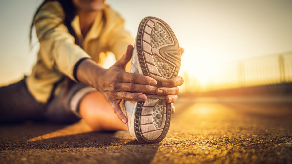 Close-up of athlete's sports shoe during stretching exercises on a road at sunset.