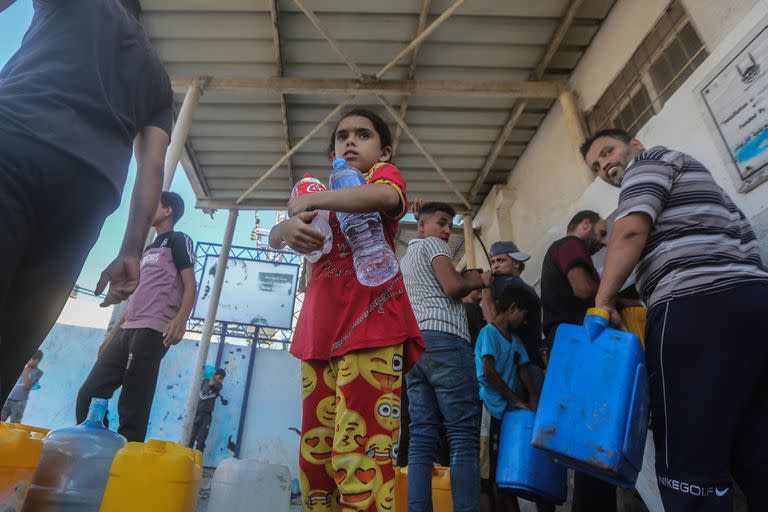 Los palestinos llenan contenedores con agua potable desde un vehículo de distribución de agua, en medio de la crisis hídrica por los bombardeos israelíes a la Franja de Gaza