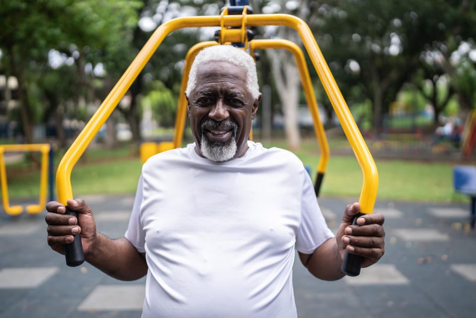 A senior man smiles while using outdoor gym equipment at a park