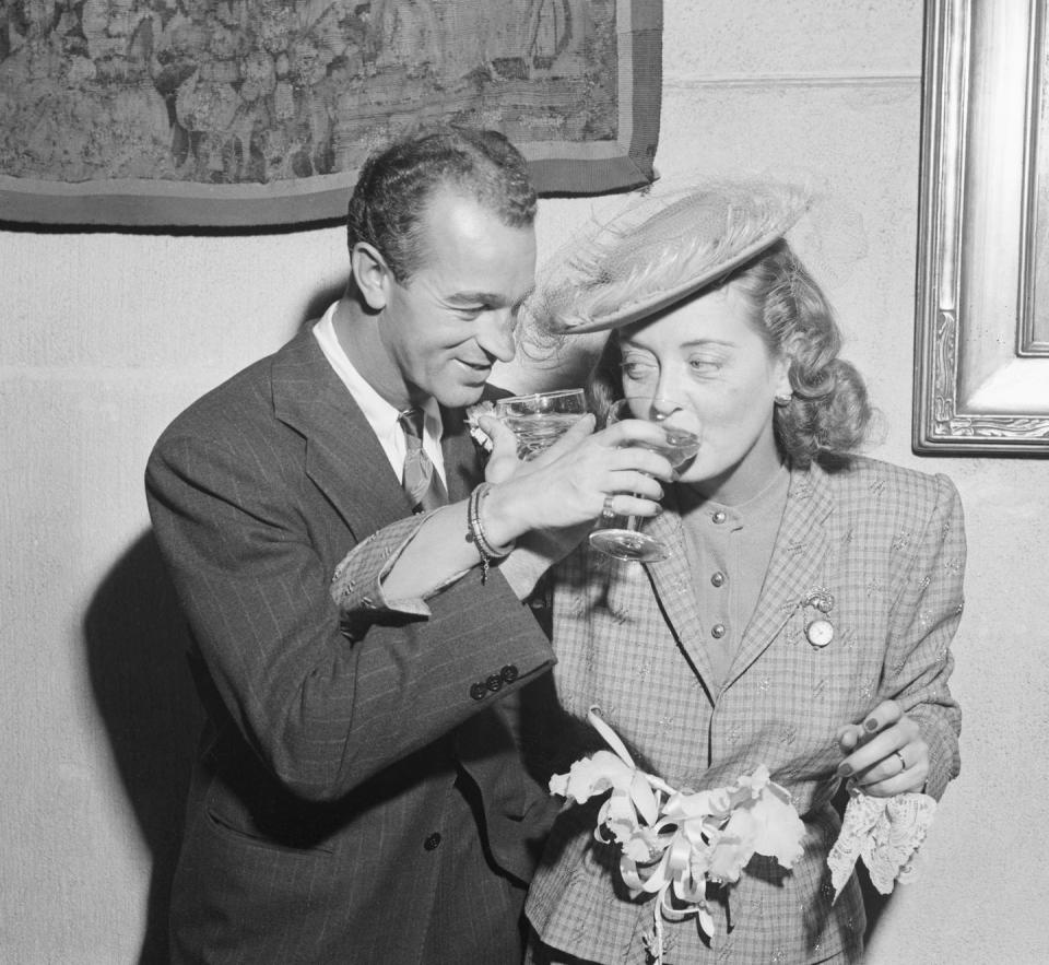 1945: Bette Davis and her third husband lock arms in a champagne toast