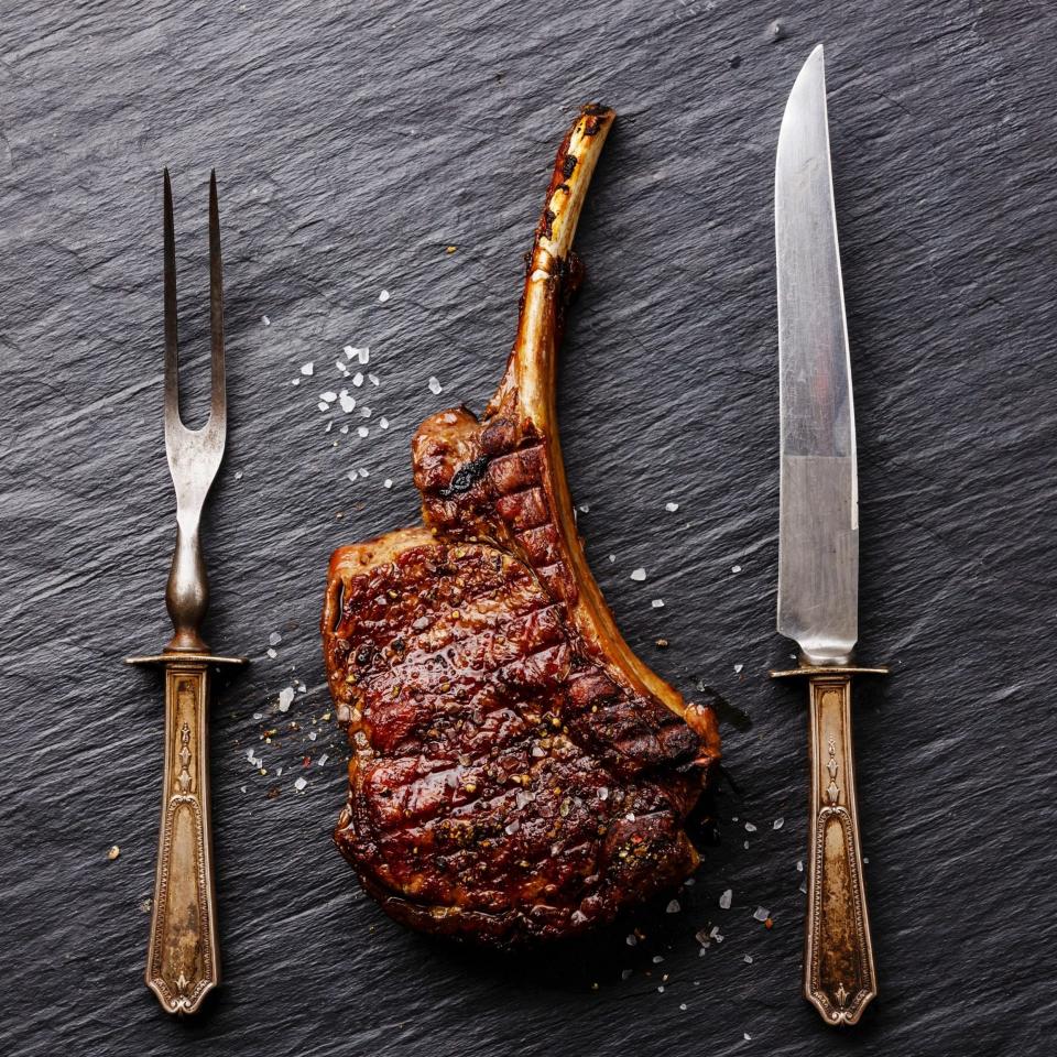 Roasted beef Rib on bone with knife and fork carving set on black stone slate