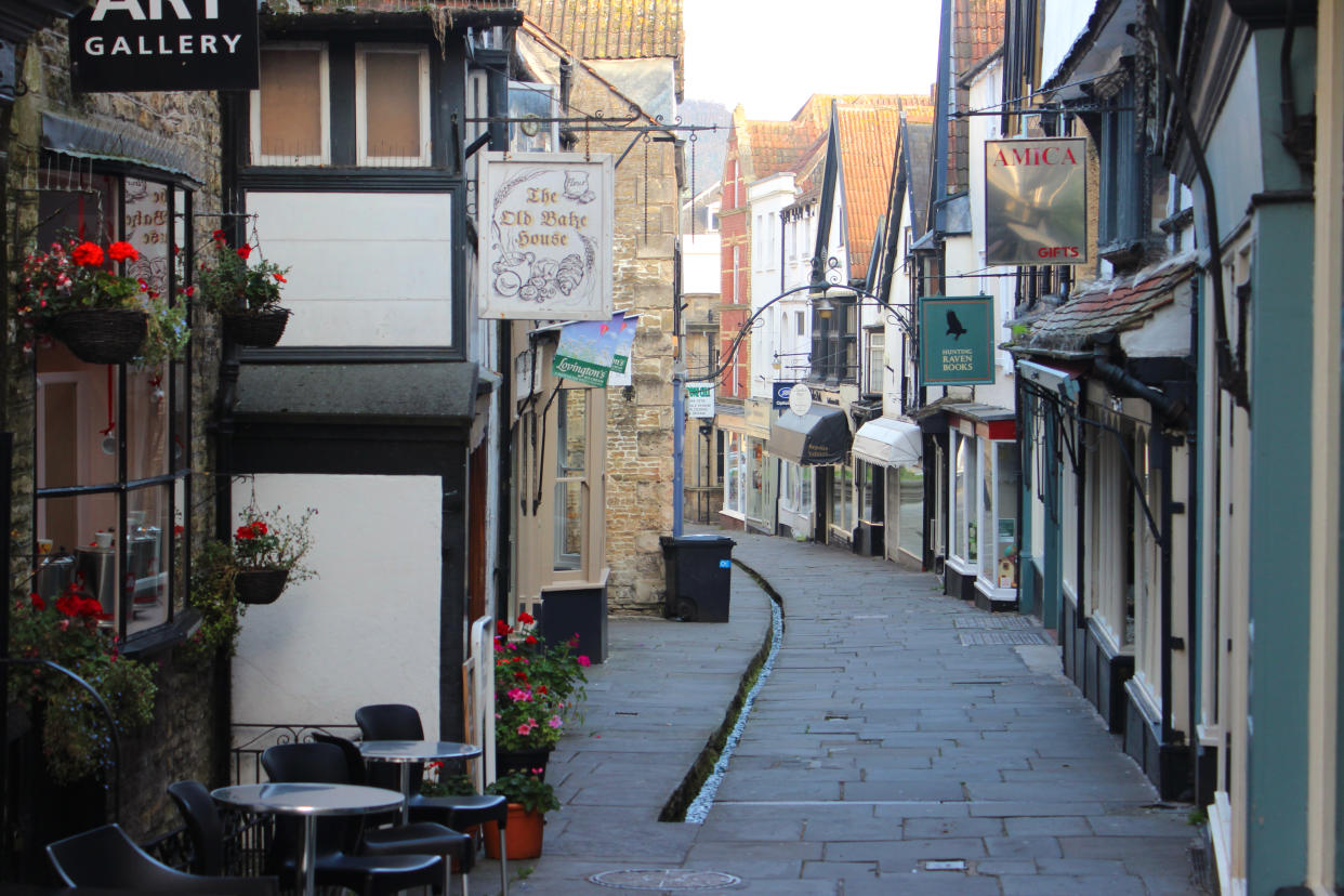 Frome, Somerset, England, UK - September, 11 2014: Image of historic medieval shops and houses lining the pedestrianised, flagstone shopping street of Cheap Street, located in the historic market town of Frome, Somerset, England.  This thoroughfare is particularly unusual, as it has a narrow stream / rill running through the centre of the street, fed by a nearby natural street at the top of the hill.