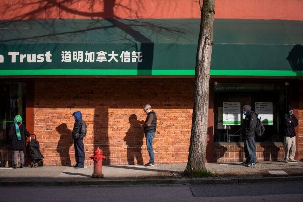 Customers wearing masks stand in a physically distanced line outside a bank in downtown Vancouver earlier this year.