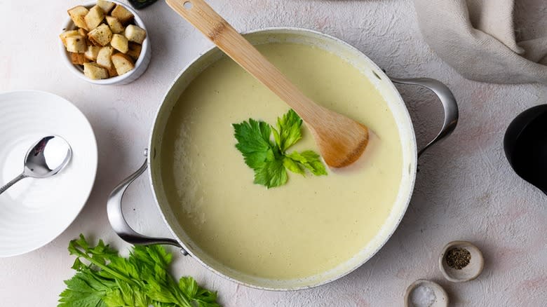 Light green cream of celery soup in a pot with wooden spoon