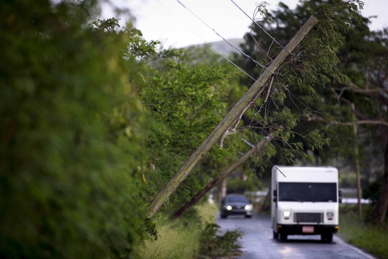 A white truck passes a dangerously slanting telephone pole leaning over the road.