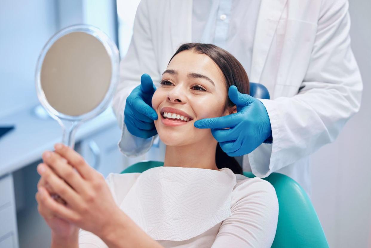 A young woman holding a mirror up to her face while a dentist shows her her teeth.