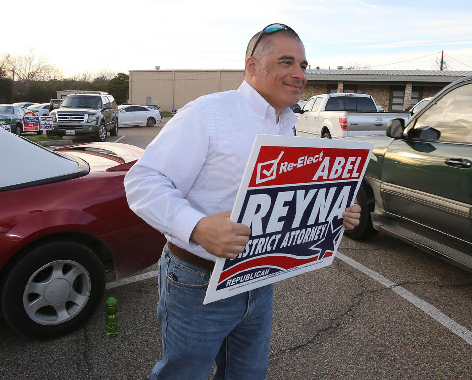 FILE - In this March 6, 2018 file photo, former McLennan County District Attorney Abel Reyna holds up a campaign sign during the a primary election in Waco, Texas. His successor Barry Johnson said in a statement Tuesday, April 2, 2019, that all charges will be dropped in the 2015 shootout between rival biker gangs in Waco restaurant parking lot that left nine people dead and at least 20 injured. Johnson said any further effort to prosecute the case would be a "waste of time, effort and resources." (Jerry Larson/Waco Tribune Herald, via AP, File)