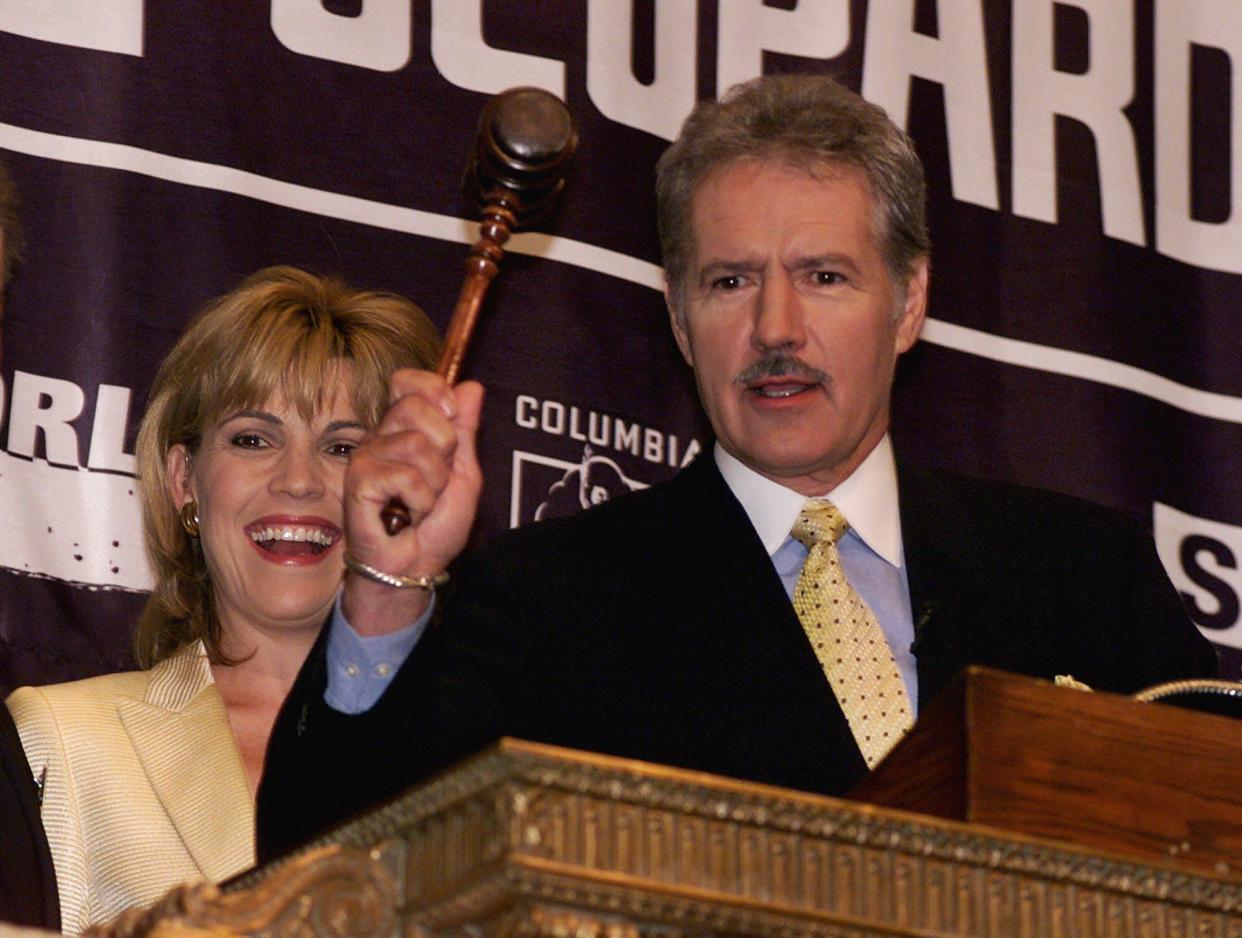 Accompanied by "Wheel of Fortune" star Vanna White (l.), Alex Trebek raises the gavel on the podium before ringing the opening bell at the New York Stock Exchange on Oct. 1, 1999.