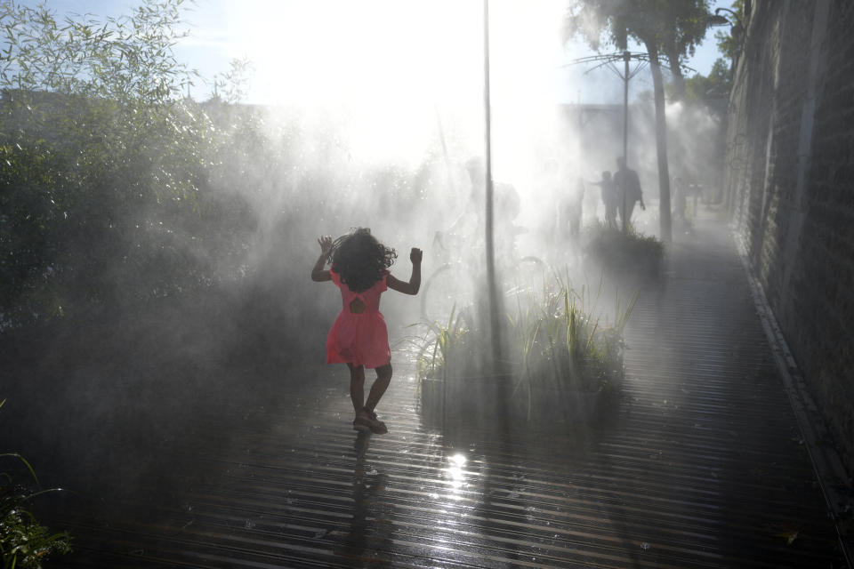 A kid walks along fresh water fogger system along the Seine river, as Europe is under an unusually extreme heat wave, in Paris, France, Tuesday, Aug. 2, 2022. (AP Photo/Francois Mori)