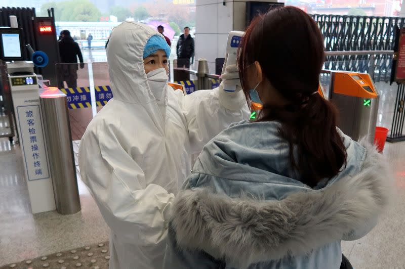 Worker in protective suits checks the temperature of a passenger arriving at the Xianning North Station on the eve of the Chinese Lunar New Year celebrations, in Xianning
