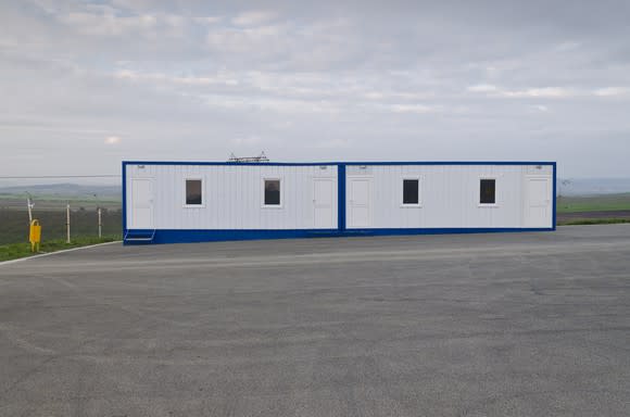 A white modular building with blue trim in a parking lot.