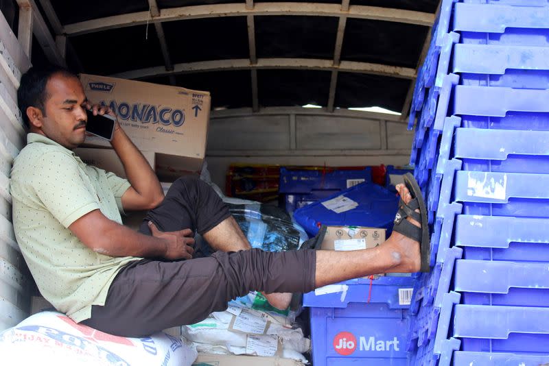 A man speaks on the phone while sitting atop sacks of consumer goods inside a delivery truck with JioMart's supplies for retailers in a crowded market in Sangli