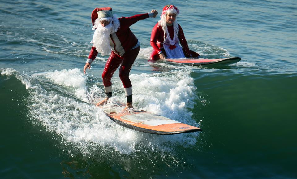 Surfing Santa, Michael Pless, 62, (L) catches a wave as his wife Jill watches, at Seal Beach , south of Los Angeles, on December 21, 2012 in California. Pless, who runs a surfing school, has been dressing up as Santa Claus and taking to the waves in costume since the 1990s.  AFP PHOTO / Frederic J. BROWNFrederic J. BROWN        (Photo credit should read FREDERIC J. BROWN/AFP/Getty Images)