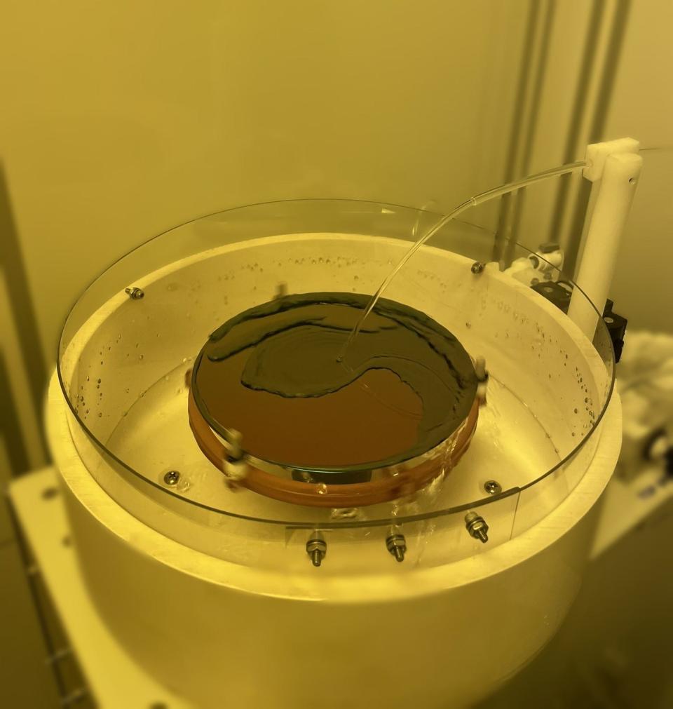 A wafer is being cleaned to remove any chemicals at the NHanced Semiconductors facility in North Carolina. The photo has a yellow tint because of the wafer's light sensitivity.