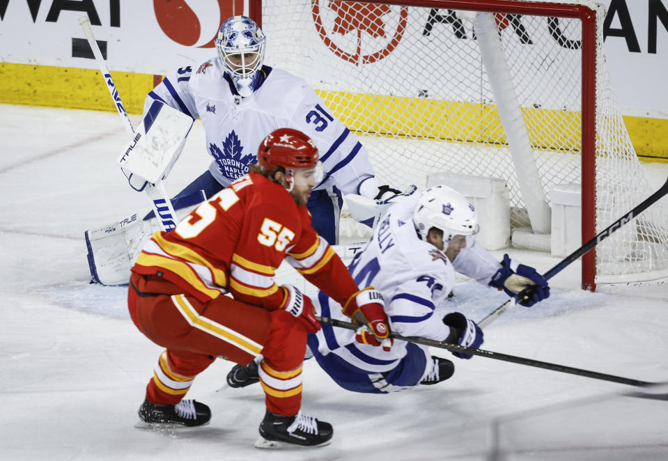 Toronto Maple Leafs goalie Martin Jones (31) looks on as Calgary Flames defenseman Noah Hanifin (55) trips Maple Leafs defenseman Morgan Rielly (44) during the second period of an NHL hockey game Thursday, Jan. 18, 2024, in Calgary, Alberta. (Jeff McIntosh/The Canadian Press via AP)