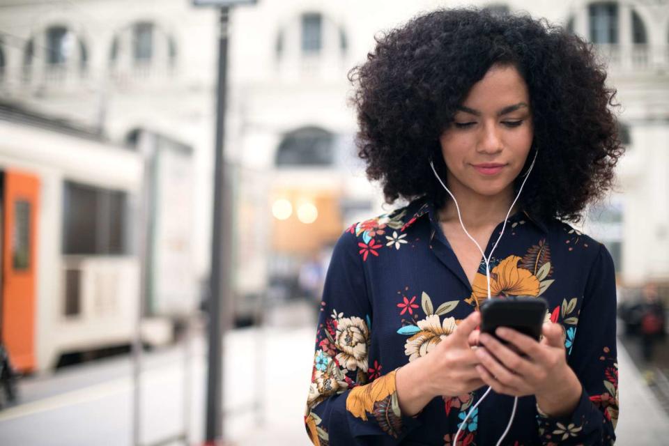 Smiling woman with curly hair using mobile phone at the train station.