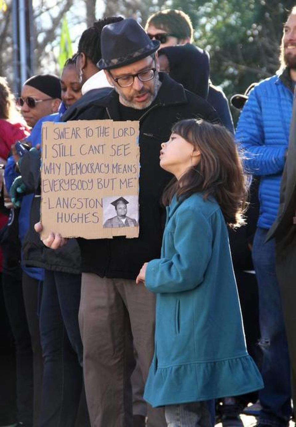 Orange County Commissioner Mark Dorosin, with friend Sophia Herbst, 6, holds a sign bearing a quote from poet and activist Langston Hughes. More than 100 people attended the rally on Peace and Justice Plaza before a service at First Baptist Church.