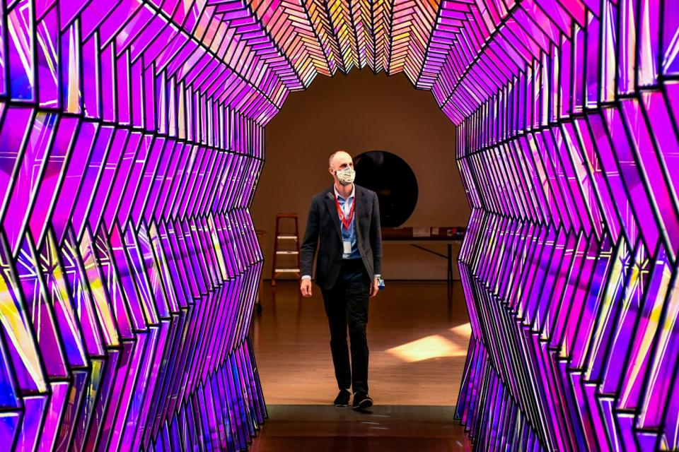 A man stands in a tunnel made of panels of purple glass.