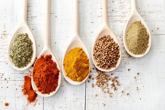 Five wooden spoons with different spices piled on them