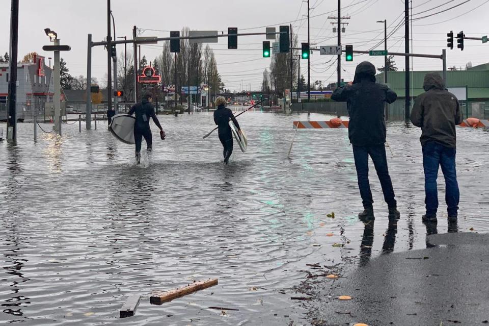 Caylon Coomes, second from left, and another man prepare to paddleboard in floodwaters on city streets in Bellingham Monday, Nov. 15. Widespread flooding in the Pacific Northwest amid days of heavy rainfall caused people to evacuate their homes, stranded drivers, and closed businesses, roads and schools.
