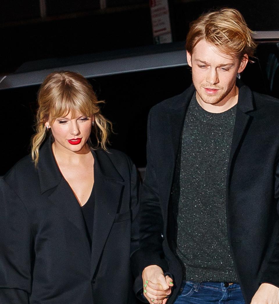 Taylor Swift in a sparkly outfit and Joe Alwyn in a black coat holding hands