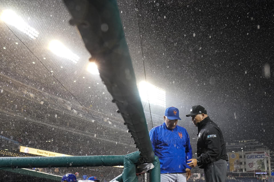 New York Mets manager Buck Showalter, left, and umpire Mark Carlson talk as a rain delay is declared during the ninth inning of a baseball game against the Washington Nationals at Nationals Park, Friday, April 8, 2022, in Washington. (AP Photo/Alex Brandon)