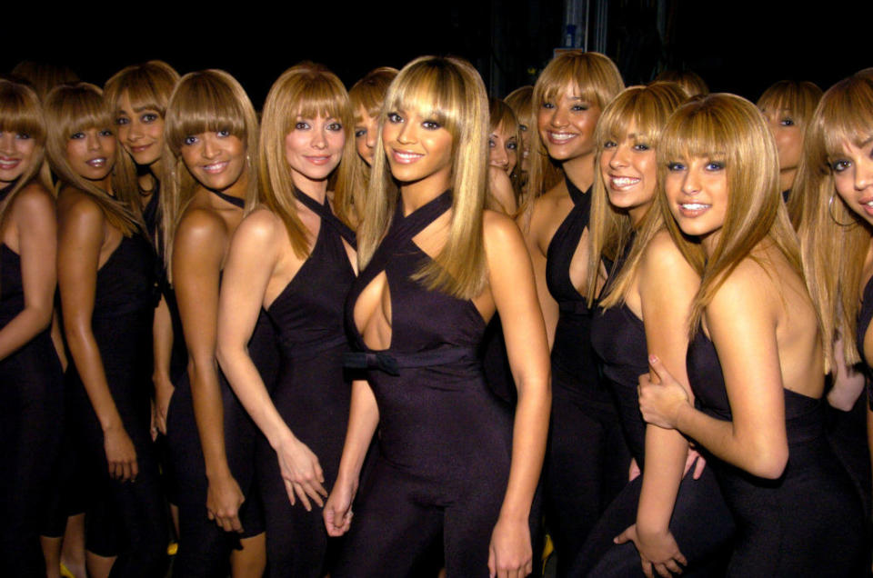 Beyoncé is smiling and surrounded by women with similar hairstyles and outfits