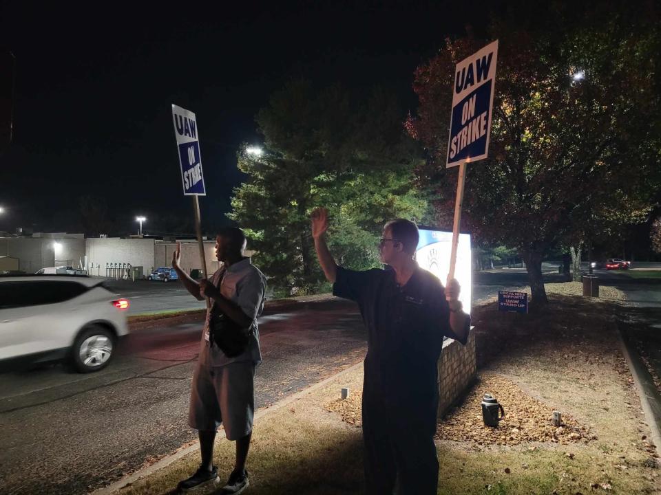 Clay Andrews, a machine repairman, and David Fagan, who works in CSS machining, wave to vehicles driving by UAW Local 1853 on Saturday night in Spring Hill.
