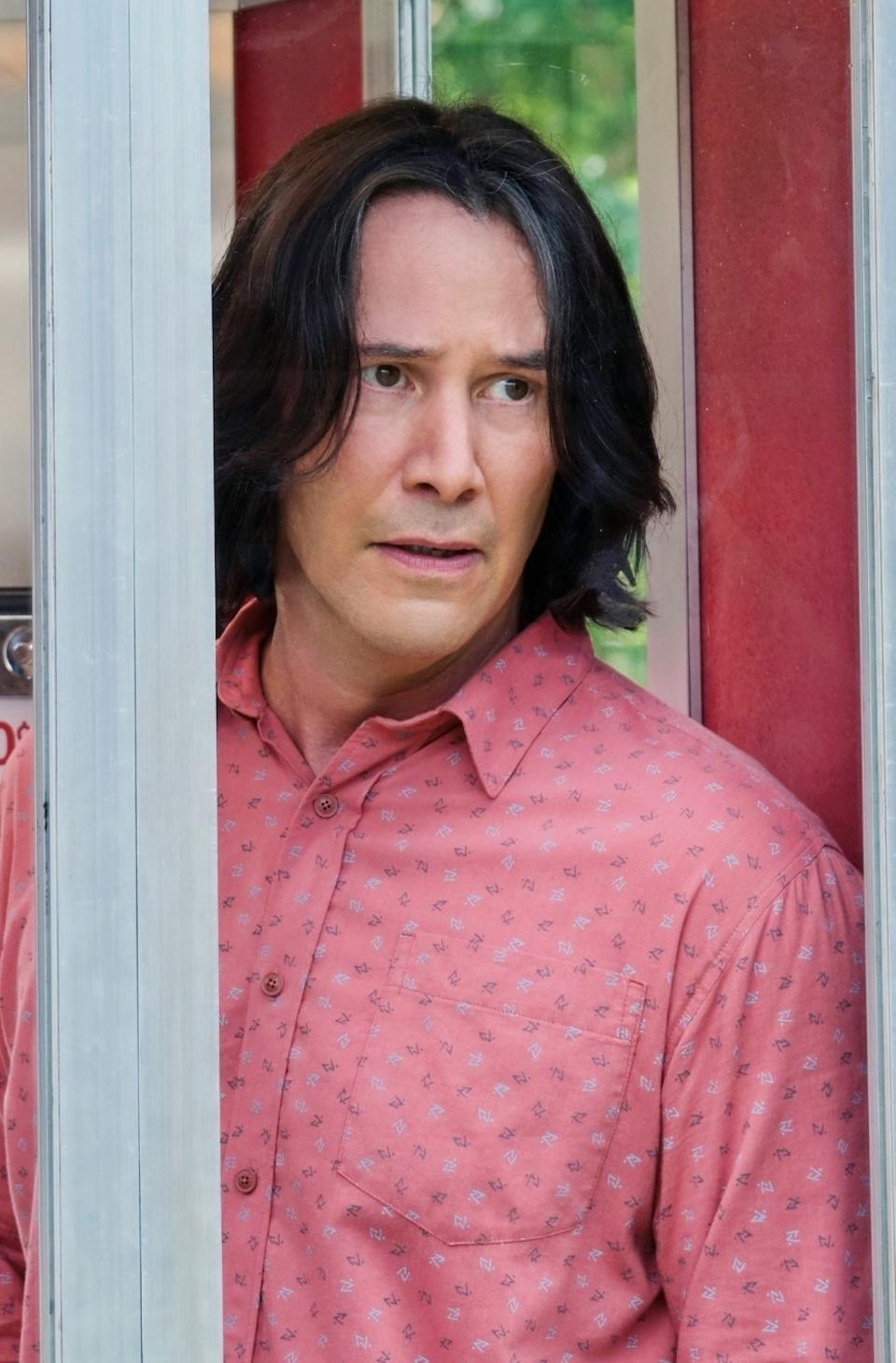 Keanu Reeves standing in a phone booth looking confused