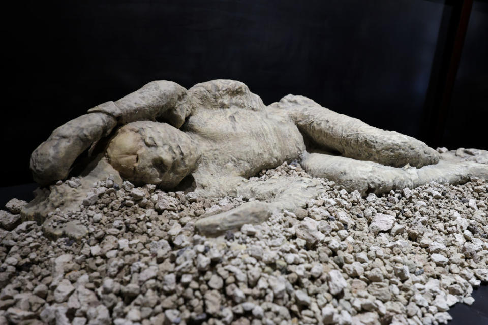 A plaster cast of a victim from Pompeii lying on their side, surrounded by volcanic debris