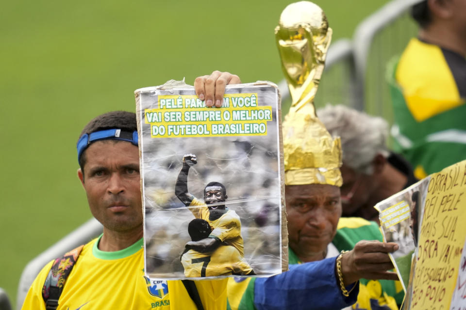 Fans hold up photos of the late Brazilian soccer great Pele as they line up at Vila Belmiro stadium where his body lies in state, to pay their last respects in Santos, Brazil, Monday, Jan. 2, 2023. (AP Photo/Andre Penner)