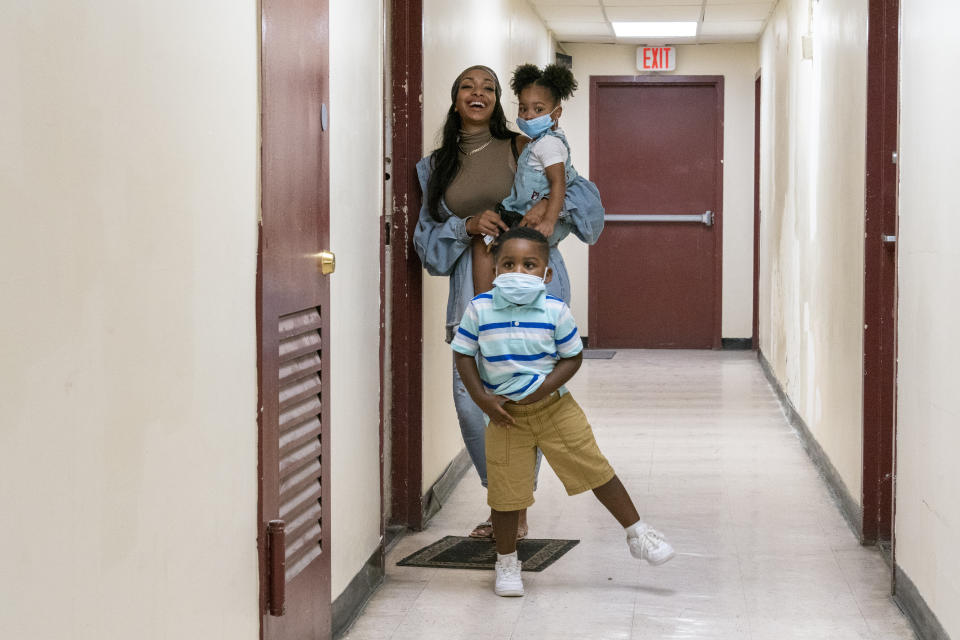 Katherine Guzman, left, holding Jazzmyn and Zavion wait in the hallway of their building while waiting for their sister Jennifer to go out for ice cream, Thursday, Sept. 17, 2020, in Newark, N.J. Four-year-old Zavion and 2-year-old Jazzmyn have been taken in by the oldest of Lunisol Guzman's other three children, Katherine and Jennifer, after she died from symptoms of coronavirus. Lunisol Guzman had adopted them when she was in her 40s. (AP Photo/Mary Altaffer)