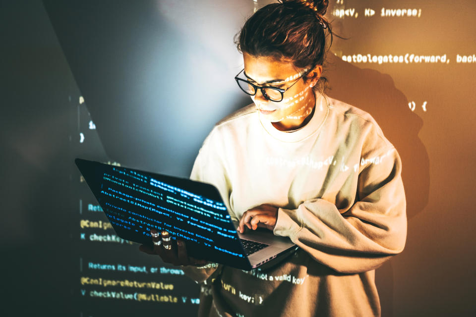 A woman in casual attire focuses on her laptop, surrounded by projected lines of computer code, illustrating a tech-savvy work environment