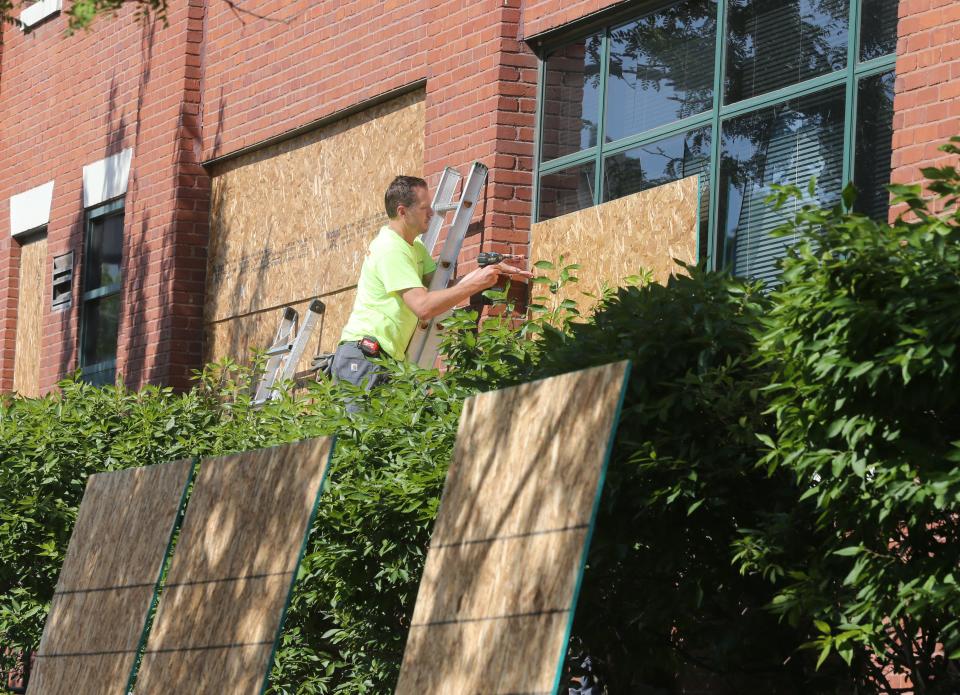 A worker from Taylor Cos. of Ohio secures a sheet of plywood to one of the 25 windows on the AES Building on South Main Street broken by protesters on July 4.