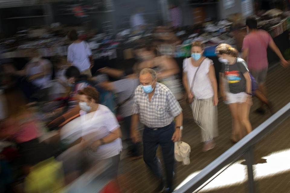 Customers wearing face masks walk past a stall in a market in Barcelona on Wednesday, July 8, 2020. Spain's northeastern Catalonia region will make mandatory the use of face masks outdoors even when social distancing can be maintained, regional chief Quim Torra announced Wednesday. (AP Photo/Emilio Morenatti)