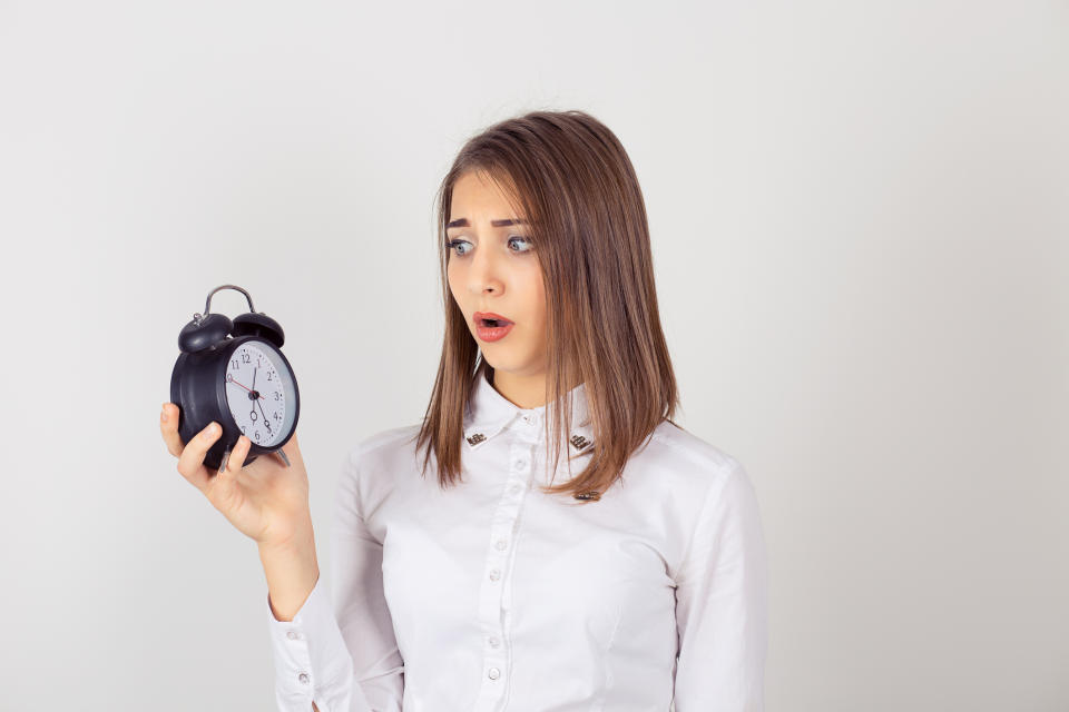Young businesswoman with alarm clock in hand, looking worried. 