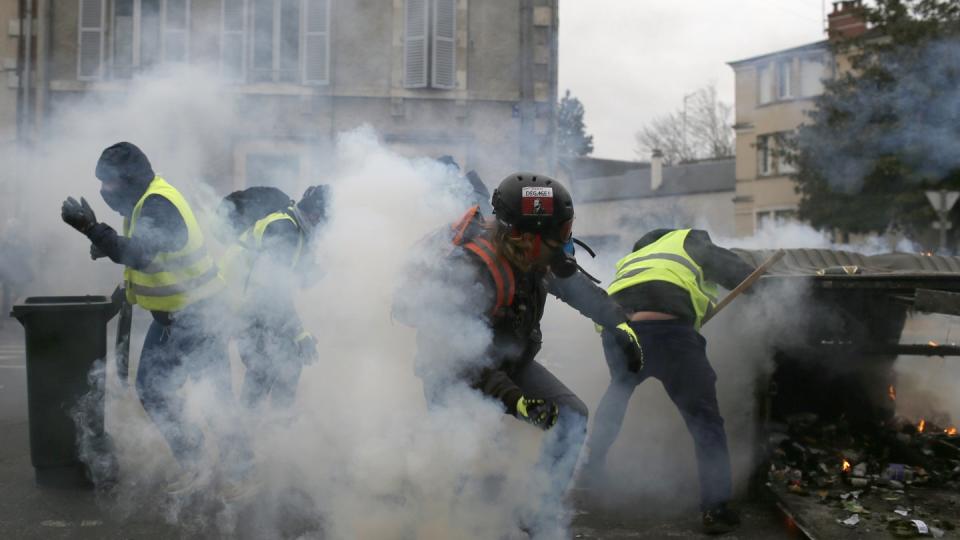 Teilnehmer einer Demonstration der «Gelbwesten» gehen in Bourges hinter ihren Barrikaden in Deckung, als Polizisten Tränengas einsetzen. Foto: Rafael Yaghobzadeh/AP