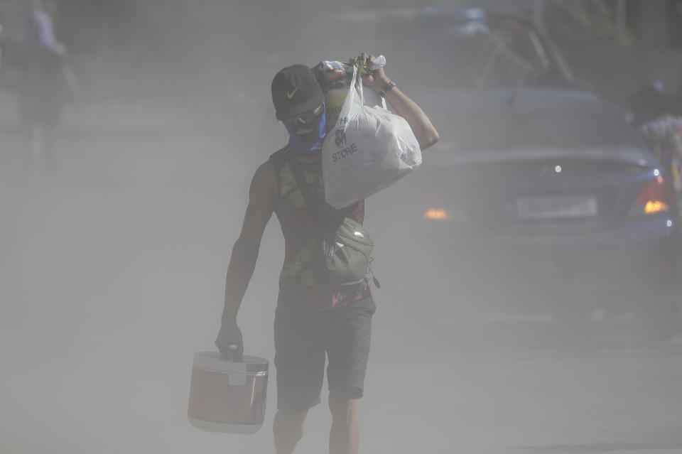 Un hombre camina con sus pertenencias entre densas nubes de ceniza levantadas al paso de gente y vehículos, mientras las autoridades aplican una evacuación total de vecinos que viven cerca del volcán Taal, en la localidad de Agoncillo, provincia de Batangas, en el sur de Filipinas, el jueves 16 de enero de 2020. (AP Foto/Aaron Favila)