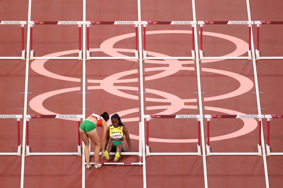 Luca Kozak of Team Hungary helps Yanique Thompson of Team Jamaica after they fell during the 100m Hurdles semifinal at the Tokyo Olympics.