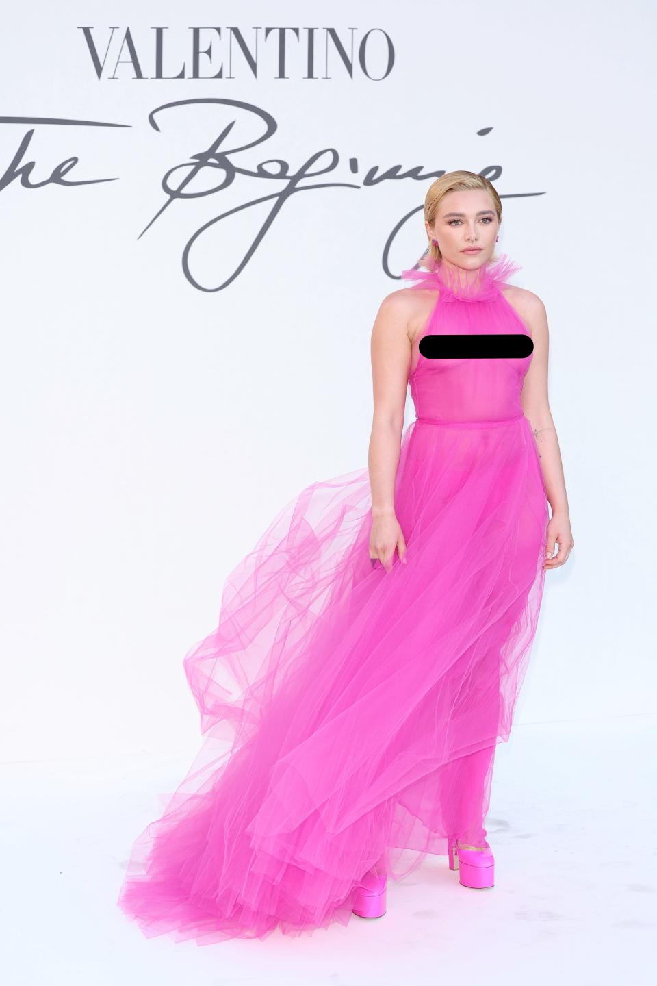 Florence Pugh stands in a pink, sheer dress in front of a white backdrop.