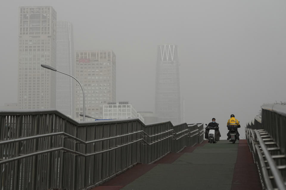 Delivery workers ride on an overhead bridge against the office buildings in the central business district shrouded by sandstorm in Beijing, Monday, Dec. 12, 2022. China will drop a travel tracing requirement as part of an uncertain exit from its strict "zero-COVID" policies that have elicited widespread dissatisfaction. (AP Photo/Andy Wong)