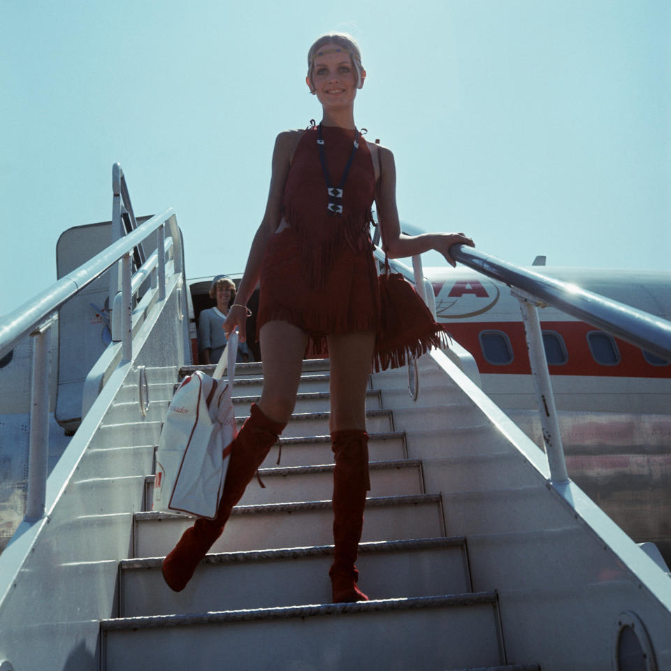 Twiggy disembarks from an aircraft in a red suede velvet outfit.