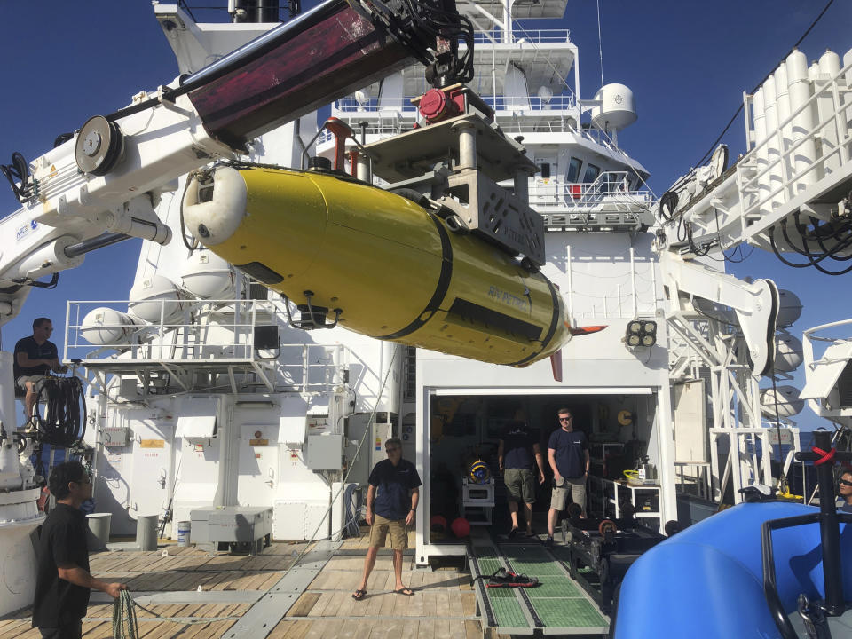 A yellow autonomous underwater vehicle on the back of a larger boat. 