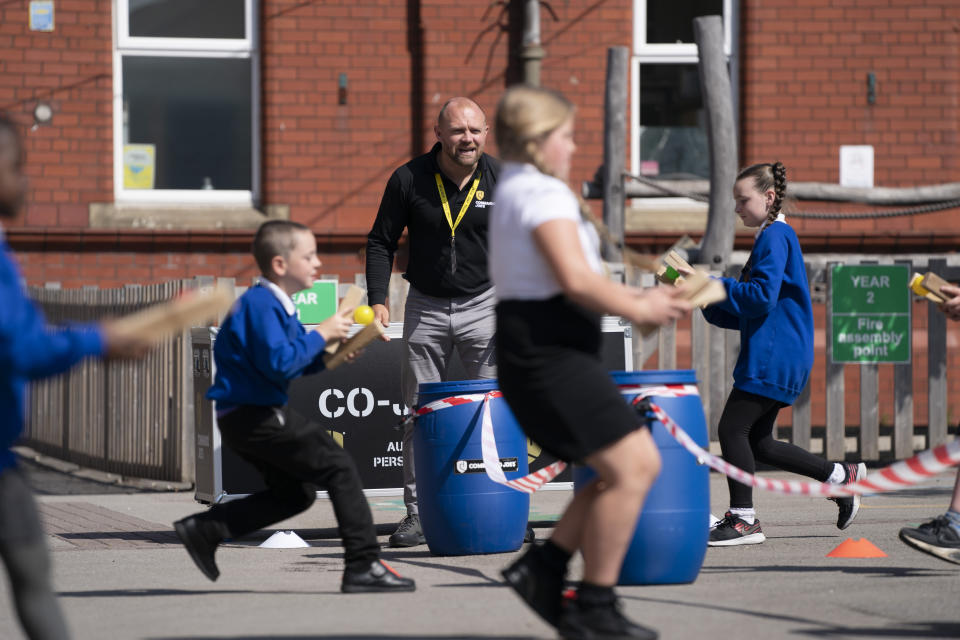 Children at Seymour Road Academy take part in a Commando Joe's character education program run by former soldier Mike Hamilton, center, during the coronavirus outbreak in Manchester, England, Wednesday May 20, 2020. Hamilton, who served with a bomb disposal unit in Afghanistan and Iraq, is working with several children in a schoolyard in Manchester, England. The mission: Picking up the virus - a small ball - with wooden blocks, racing to a bin, and dropping the ball inside before pretending to wash their hands. (AP Photo/Jon Super)