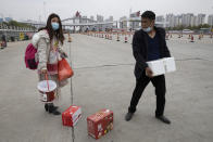 In this Thursday, April 2, 2020, photo, a man assists a woman with her belongings as they cross the expressway gate at the border of Wuhan city in central China's Hubei province. Millions of Chinese workers are streaming back to factories, shops and offices but many still face anti-coronavirus controls that add to their financial losses and aggravation. In Wuhan police require a health check and documents from employers for returning workers. (AP Photo/Ng Han Guan)